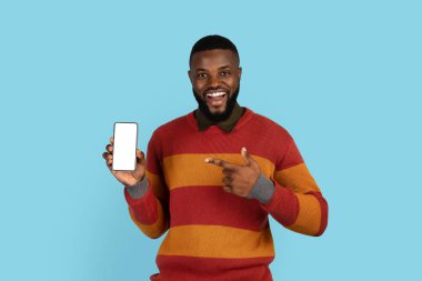 Mobil Teklif. Yakışıklı siyah erkek elinde boş beyaz ekranla telefonu işaret ediyor, gülümseyen Afrikalı Amerikalı bir adam yeni bir uygulama ilanı veriyor, mavi arka planda tek başına duruyor,
