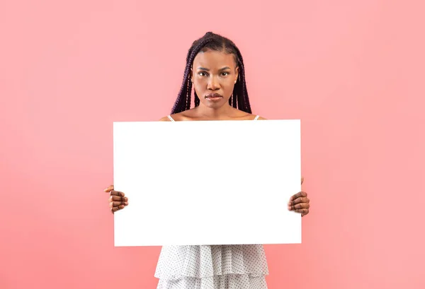 严肃的年轻黑人女人拿着空白的纸横幅 在粉红的背景上设计造型 美丽的非洲裔美国女性展示空白海报 广告空间 — 图库照片