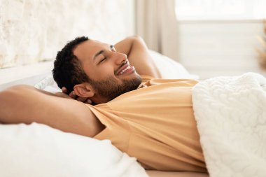 Dinlenme ve dinlenme. Mutlu Arap adam dinleniyor, gözleri kapalı uzanıyor, ellerini başının arkasında tutuyor ve evdeki modern yatak odasında uyuyor. Sağlıklı Uyku Konsepti. Yan Görünüm