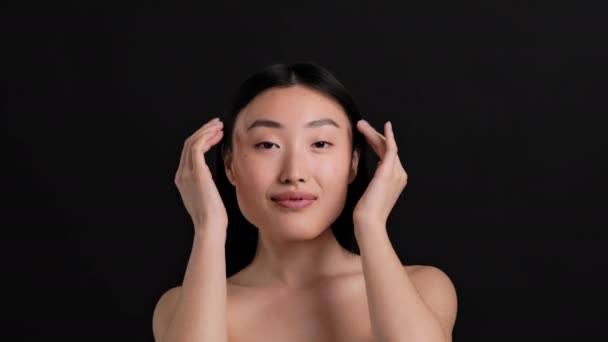 年轻迷人的亚洲女人摸着她的脸和脖子 喜欢柔软的皮肤 黑色的工作室背景 慢动作 — 图库视频影像