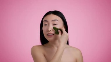 Evdeki güzellik hizmetleri. Çıplak omuzlu genç Asyalı bir kadının stüdyo portresi. Gouache taşıyla cilt masajı yapıyor. Kameraya gülümsüyor.