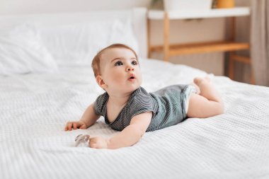 Çocuk bakımı konsepti. Beyaz çarşafların üzerine uzanmış bebek tulumu giyen şirin bir bebek. Yukarı bakıyor, kopya odası. Güzel bebek yatak odasında yatakta emekliyor.