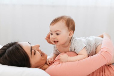 Annelik kavramı. Sevgi dolu genç anne evde sevimli çocuğuyla oynuyor, yatakta dinleniyor ve tatlı bebekle bağ kuruyor, boşluğu kopyalıyor.