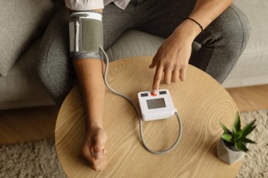 Evinde tonometre kullanan tanınmayan siyah bir hastanın en üst görüntüsü. Yakın plan. Kan basıncını ölçen genç Afrikalı Amerikalı bir adam, içeride kendi kendini kontrol ediyor.