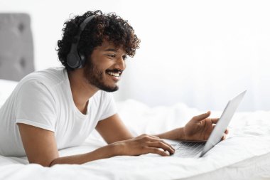 Mutlu kıvırcık sakallı, genç doğu çocuğu. Laptop ve kablosuz kulaklık kullanarak hafta sonunun tadını çıkarıyor. İnternette film izliyor ya da video oyunları oynuyor.