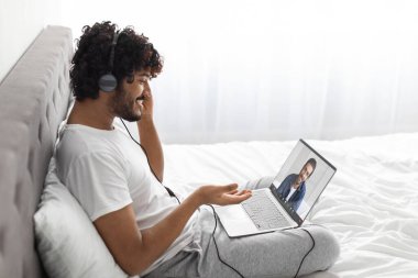 Mutlu bir milenyum doğulu adam evinde dizüstü bilgisayar ve kulaklık kullanarak arkadaşlarıyla online parti veriyor. Hintli adam kucağında not defteriyle oturuyor.