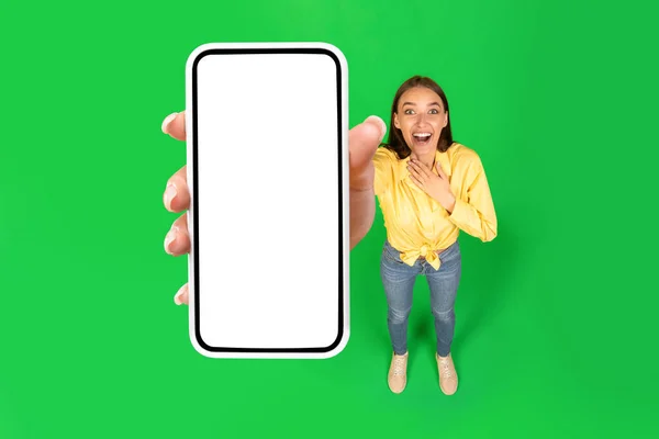 兴奋地展示大手机与空屏幕微笑站在工作室的绿色背景 Lady Advertising Mobile Offer Application 高角度 莫科普 — 图库照片
