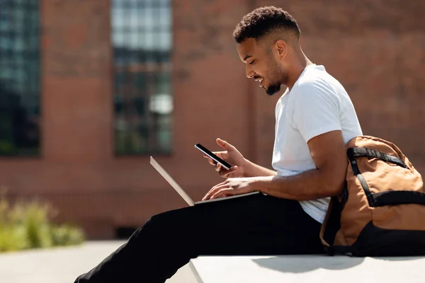 Jovem Afro Americano Com Laptop Sentado Livre Usando Smartphone Navegar — Fotografia de Stock