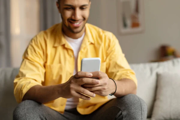快乐的年轻非洲裔美国人坐在沙发上 拿着智能手机 上网或上网学习 浏览社交网络 在家里看视频 有选择地集中注意力 复制空间 — 图库照片