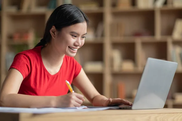 微笑着快乐的日本少女在餐桌边做作业 房间里有笔记本电脑 家庭视频课程 现代技术教育 因Covid 19大流行病而在网上举办的网络研讨会 — 图库照片