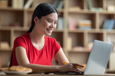 Masada dizüstü bilgisayarda yazı yazan güzel Asyalı bir kadının oturma odasında çalışmasına sevindim. Eğitim kumandası, sosyal ağlar, blog ve sohbet, modern cihaz, covid-19 salgını sırasında internetten reklam ve teklif