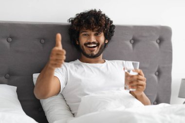 Sağlıklı, sakallı, elinde bir bardak su tutan, parmağını kaldıran, yatakta oturup kaynak suyu içen genç mutlu Hintli adam yeni güne temiz su ve fotokopi alanıyla başlıyor. Susuzluk, konsept
