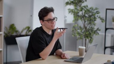 Sesli mesaj konsepti. Genç kaygısız adam akıllı telefon uygulamasına sesli mesaj kaydediyor, hafta sonu için planları tartışıyor, ofiste oturuyor, yavaş çekim, boş alan