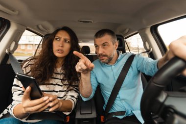 Araba Seyrüsefer Başvurusu. Şehirdeki Yeni Otomobilde Araba Kullanan Çift, Parmak Gösteren Koca, Yönünü Gösteren Cep Telefonu Kullanıyor. Sürücü kavramı için trafik uygulaması. Seçici Odaklanma