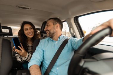 Mutlu çift yeni otomobilde oturan akıllı telefondan araba seyrüsefer uygulaması kullanıyor. Eşi, Oto ile Seyahat Eden Kocasına Cep Telefonu Gösteriyor. Araç ve Teknoloji Konsepti
