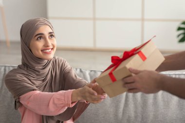 Neşeli Orta Doğulu Kadın Başörtüsü Giyiyor, Hediye Alıyor, tatilini evde koltukta oturarak kutluyor. Tanınmayan Adam Paketli Kutuyu Müslüman Kadına Veriyor. Mevcut Teslimat Konsepti