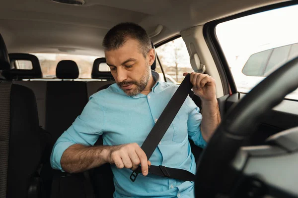 Car Driving. Middle Aged Male Driver Putting On Seat Belt Sitting In New Automobile. Auto Insurance And Transportation Safety. Vehicle Ownership Concept. Selective Focus