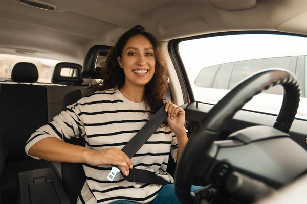 Car Driving. Arabic Female Driver Putting On Seat Belt Smiling To Camera Sitting In Auto. Brunette Young Woman Learning To Drive Posing In Vehicle. Automobile Ownership And Transportation