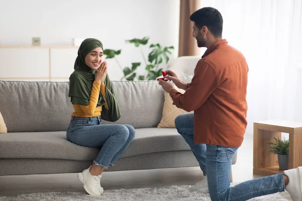 Middle Eastern Man Making Romantic Marriage Proposal Proposing To Girlfriend Offering Box With Engagement Ring Standing On One Knee At Home. Relationship And Marriage Concept.
