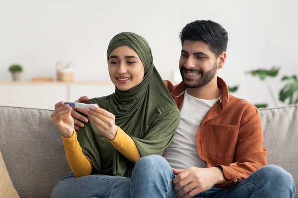 Mutlu Ortadoğu Eşleri Pozitif Öngörü Testi Sonuçlarına Bakıyorlar. Koltukta birlikte oturuyorlar ve bebek bekliyorlar. Beklentinin neşesi. Aile ve Doğum Konsepti