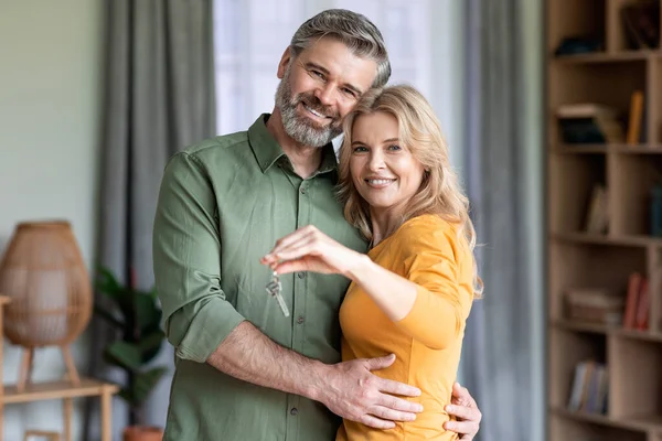 Mutlu orta yaşlı çift ellerinde ev anahtarları ve gülümseyen romantik, olgun eşler kameraya bakıyor, yeni dairelerine taşındıktan sonra içlerini zehirliyorlar.