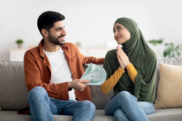 Müslüman koca, evdeki koltukta oturan minnettar eşine para veriyor. Başörtülü kadın, adamdan kendisine biraz para vermesini istiyor. Mali ve Aile Bütçesi Konsepti