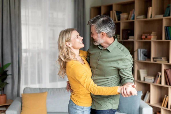 Romantik orta yaşlı çift oturma odasının içinde dans ediyor, neşeli olgun eşler el ele tutuşuyor ve birbirlerine gülümsüyor, birlikte vakit geçiriyorlar, boşluğu kopyalıyorlar.