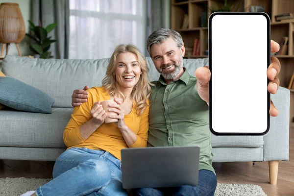 Harika bir uygulama. Orta Çağ Eşleri, evde dizüstü bilgisayarla otururken Beyaz Ekran 'da Beyaz Ekran' da Boş Akıllı Telefonları Gösteriyorlar, Mutlu Olgun Çiftler Yeni Mobil Uygulama, Mobil Mobil Mobil Uygulama