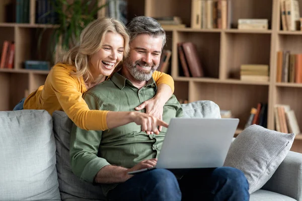 快乐的中年夫妇 膝上型电脑有乐趣和放松在家里 快乐的成熟丈夫和妻子一起看喜剧电影 女人在设备屏幕上指点和大笑 复制空间 — 图库照片