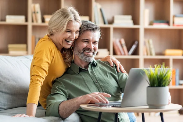 快乐的中年夫妇一边在笔记本电脑上一起上网 一边在家里放松 快乐成熟的丈夫和美丽的妻子在客厅里和电脑一起休息 复制空间 — 图库照片
