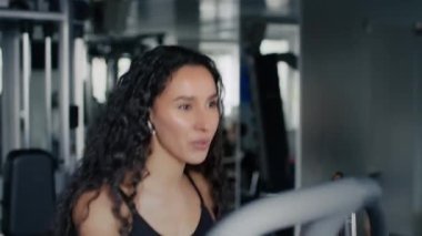 Dinamik spor eğitimi. Spor salonunda eliptik eğitim aparatları üzerinde egzersiz yapan, kablosuz kulaklıklarla enerjik müziğin keyfini çıkaran genç aktif kadının portresini kapat.