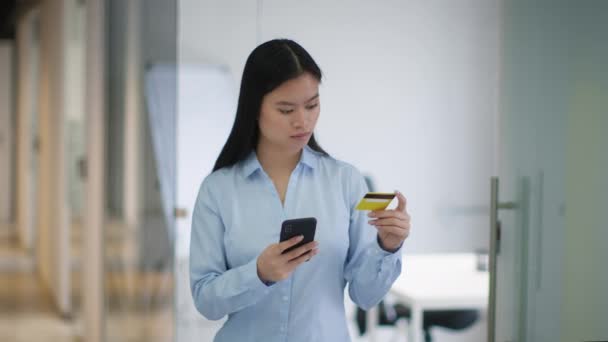 移动银行概念 年轻而严肃的亚洲女经理用智能手机和信用卡进行网上交易 站在办公室 动作缓慢 — 图库视频影像
