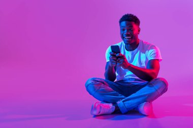Bin yıllık Afro-Amerikan bir adam akıllı telefonuyla bacak bacak bacak üstüne atmış, sosyal medyada sörf yapıyor, neon ışıkta arkadaşlarıyla sohbet ediyor, mekanı kopyalıyor. Havalı siyah adam cep telefonu kullanıyor.
