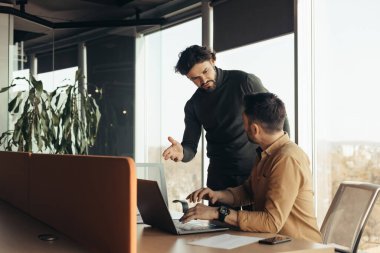 İş adamı, iş yerindeki dizüstü bilgisayarla proje detaylarını ortağına anlatıyor. Girişimciler iş toplantısı yapıyor, ofis alanındaki yeni stratejileri ve fikirleri tartışıyorlar.