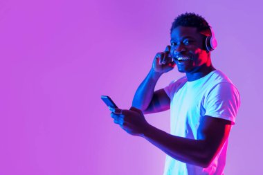 Kablosuz kulaklıklar takmış, neon ışıkta akıllı telefon kullanan neşeli, bin yıllık siyah bir adam. Yakışıklı Afrikalı genç Amerikalı adam yeni mobil müzik uygulamasını kontrol ediyor, sesli kitaptan keyif alıyor.