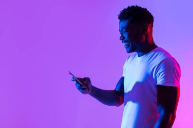 Akıllı telefon kullanan, çalışan ya da uzaktan çalışan, sosyal medyada neon ışığı altında yer alan, fotokopi çeken neşeli genç bir zenci. Mobil cihazlı Afrikalı Amerikalı adam yeni uygulamayı kontrol ediyor