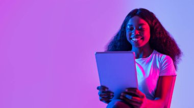 Tablet kullanan neşeli genç siyahi kadın portresi, çalışmak ya da uzaktan çalışmak, neon ışıkta online görüşme, boş alanlı pankart tasarımı. Milenyum bayanı yeni uygulamayı kontrol ediyor
