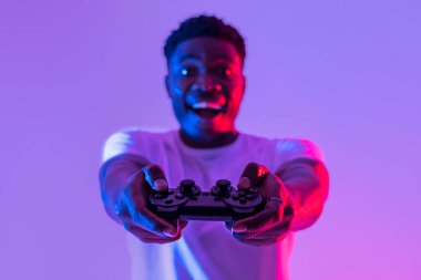 Oyun çubuğuyla neon ışıkta video oyunu oynayan mutlu, genç siyahi adam, seçici odaklanma. Çevrimiçi oyun şampiyonasına katılan denetimci Afrikalı Amerikalı oyuncu. Modern hobiler
