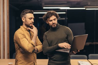 Erkek iş arkadaşları ortak iş projesinde çalışıyorlar, laptop ekranına bakıyorlar, modern ofiste geliştirme stratejileri ve fikirleri tartışıyorlar. Şirket yaşam tarzı, işbirliği, iş birliği konsepti