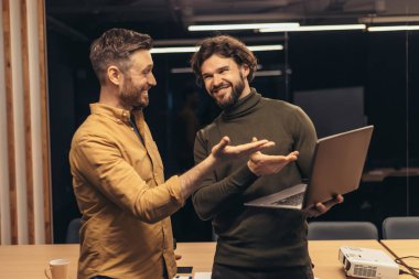 Başlangıç projesinde birlikte çalışan, fikirleri tartışan, ofiste dizüstü bilgisayar kullanan iki neşeli erkek arkadaşın portresi. Başarılı bir işbirliği ve işbirliği, takım çalışması konsepti