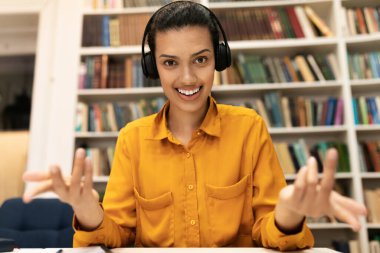 Melez ırktan bir kadının internet araması ya da sanal görüşme yaptığı, kütüphanede otururken kamerayla konuştuğu, kulaklık taktığı ve bir şey açıkladığı ön portresi.