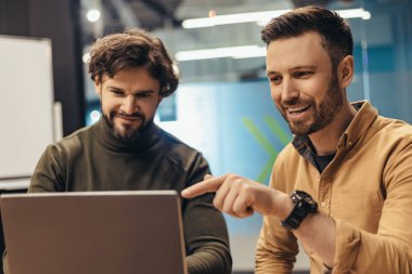 Takım çalışması, kurumsal iletişim ve iş yeri konseptinde işbirliği. Pozitif erkek meslektaşlar iş projesini tartışıyor, dizüstü bilgisayar kullanıyor, ofisteki fikirler için beyin fırtınası yapıyor.