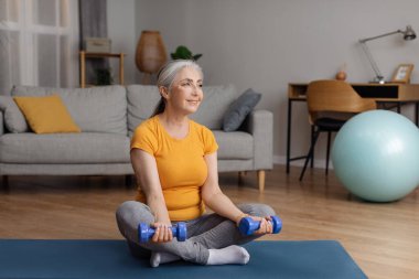 Spor kıyafetleri içinde, halterlerle egzersiz yapan, yoga minderinde oturan, fotokopi çeken formda bir kadın. Mutlu kadın ağırlık çalışıyor.