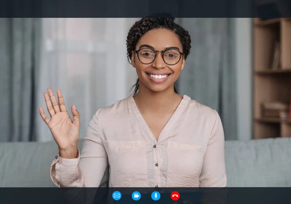 Happy african american young lady doctor in glasses waving hand at camera in clinic office interior on gadget screen with buttons. Doctor support, professional help, therapy, treatment and medicine