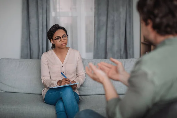 严重的年轻非洲裔美国女心理学家戴眼镜听欧洲病人在诊所的办公室内部 抑郁症 心理支持 专业帮助 心理治疗和问题 — 图库照片