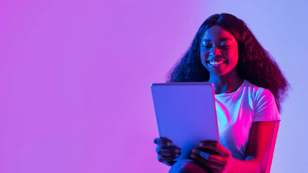 タブレットPcを使用して楽しい若い黒人女性の肖像画 勉強やリモートで作業 ネオンライトでオンライン会議を持っています 空の空間とバナーデザイン タッチパッド付きのミレニアル世代の女性が新しいアプリをチェック — ストック写真