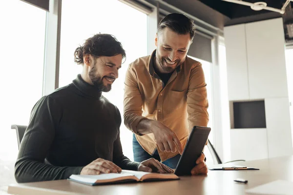 Coworking concept. Trainee working on tablet computer with his mentor, doing business research at company office, copy space. New team member communicating with experienced male colleague