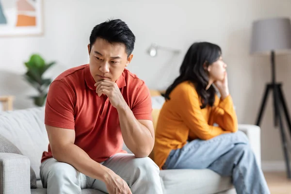 Sad asian man fighting with his lover, thoughtful korean husband and wife having crisis in relationship, sitting on sofa, thinking about divorce or family therapy, home interior