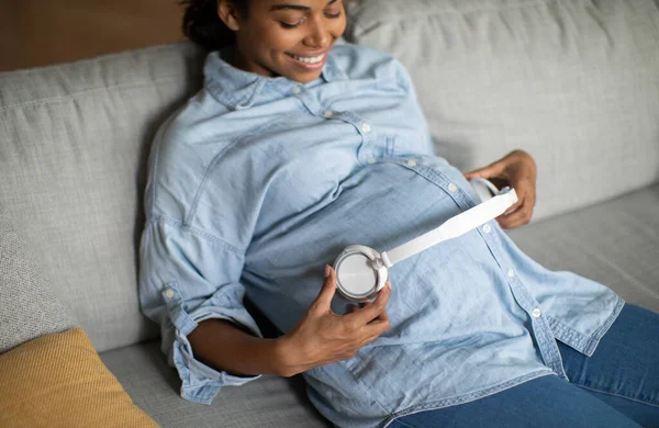 快乐怀孕的非洲裔美国女士带耳机听着轻松的音乐坐在沙发上在家里 怀孕游戏列表和放松的概念 选择性聚焦 — 图库照片