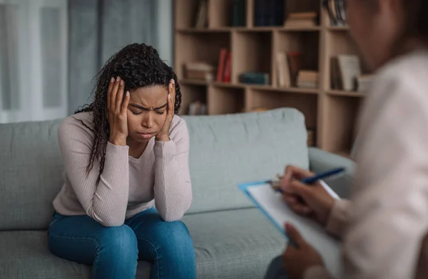 Depressed unhappy african american millennial lady crying at consultation with european psychologist in office interior. Mental problems and treatment, medical support, professional help, therapy
